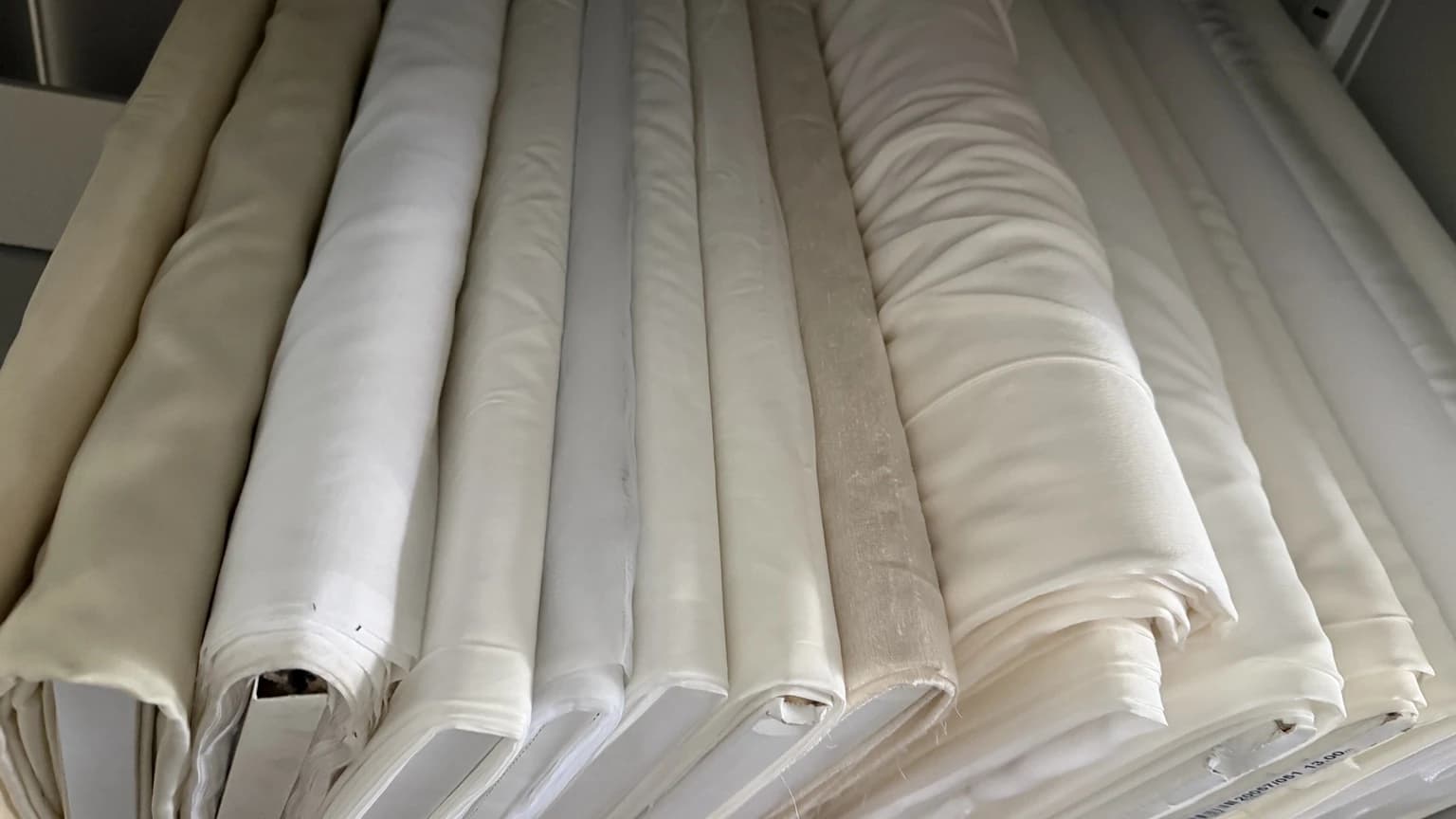 Rouleaux de tissus de l’atelier, aux nuances allant du blanc à l’ivoire et à l’écru